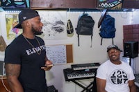 two men standing in front of a keyboard in a recording studio